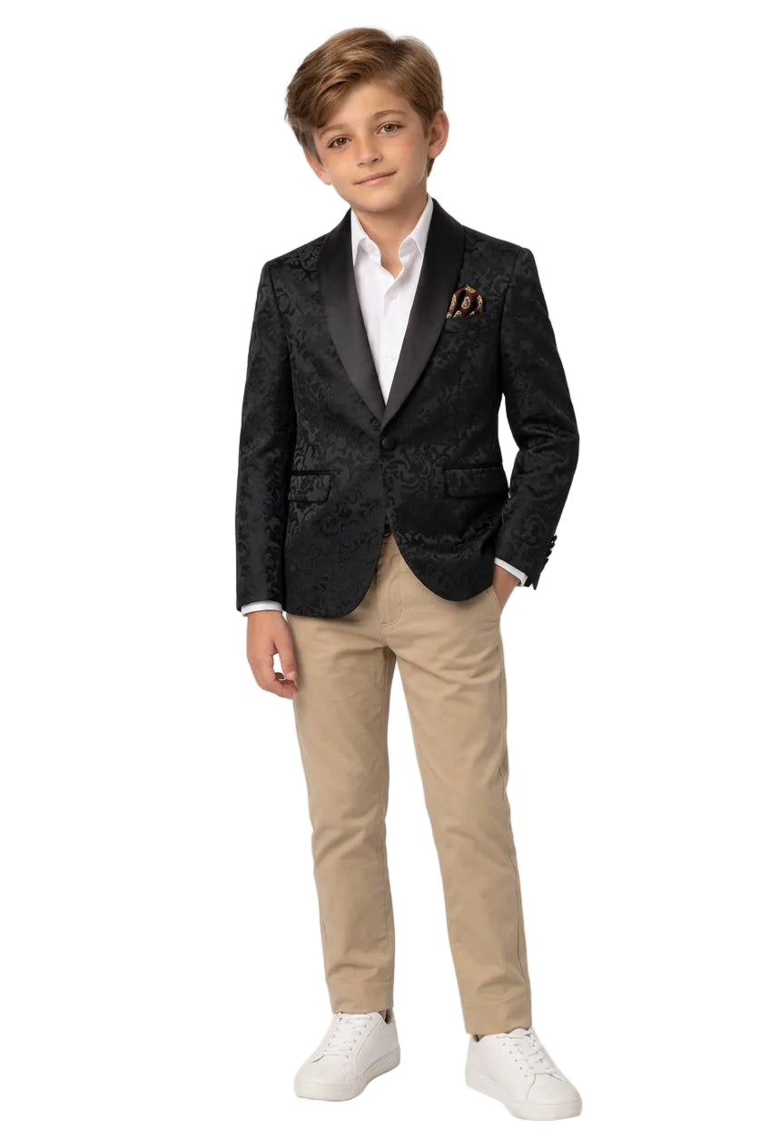 A young boy modeling a black textured blazer, white collared shirt, beige trousers, and white sneakers, standing against a seamless white studio background.