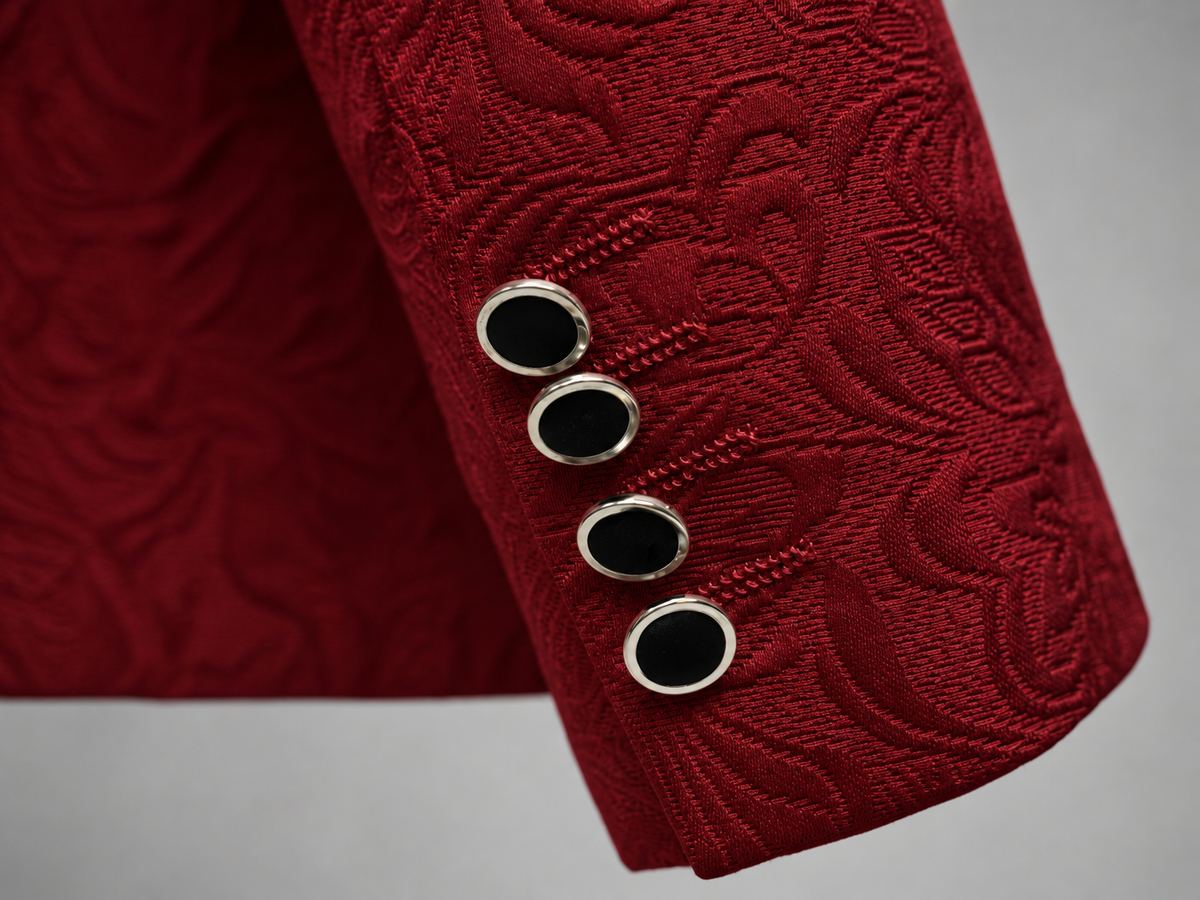 Close-up of a red textured suit jacket sleeve with four decorative oval buttons featuring black centers and silver borders, set against a neutral gray background.