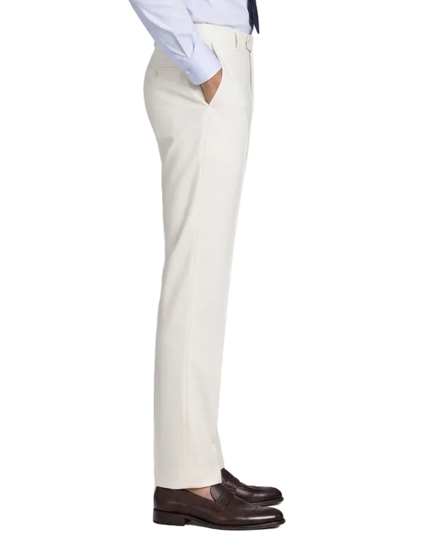 A man in a light blue dress shirt, dark tie, and white trousers stands in profile against a light gray studio background, wearing dark brown leather loafers.
