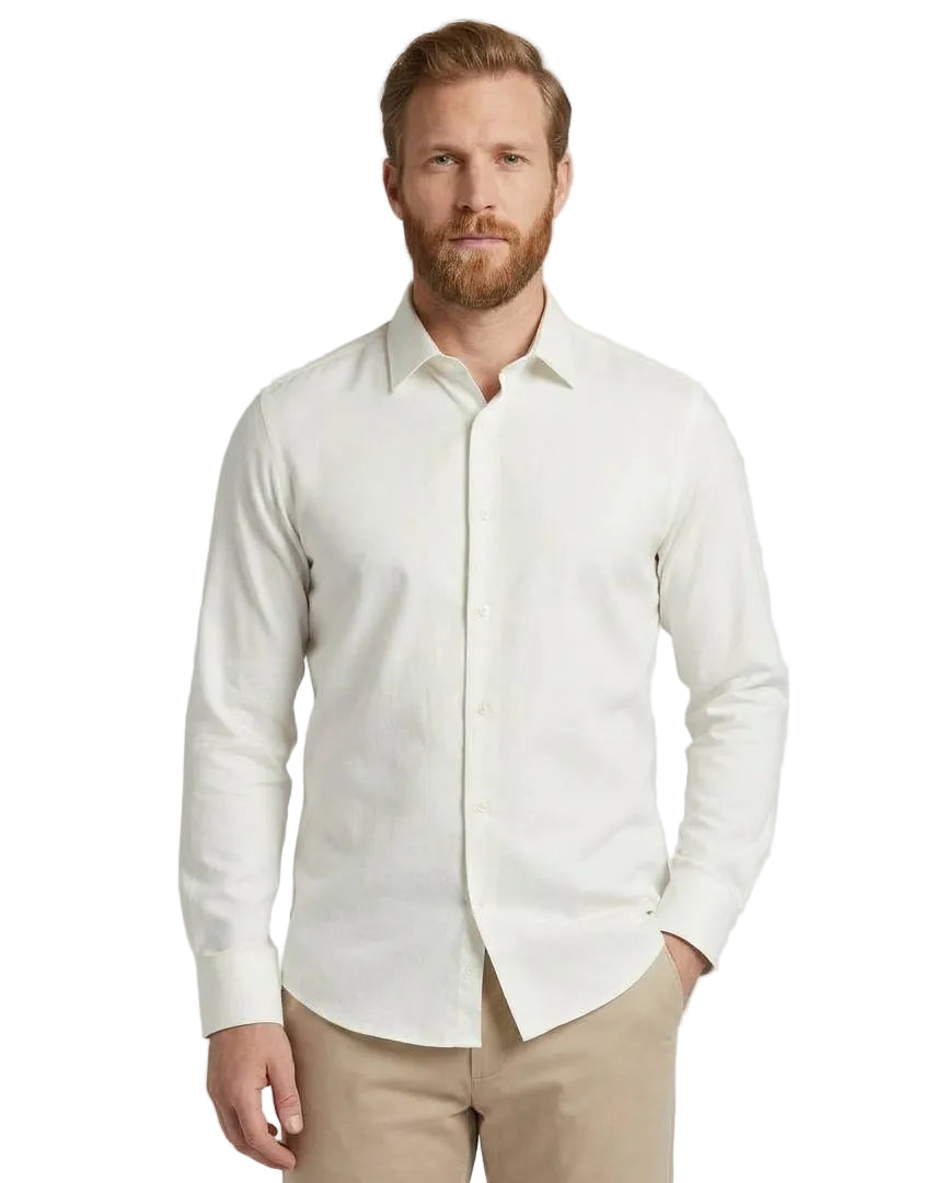 A man wearing a light cream long-sleeve button-down shirt and khaki trousers, standing against a neutral light gray studio background.