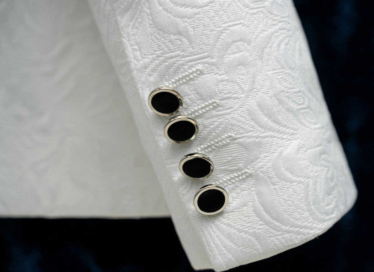 Close-up of a white textured fabric cuff with four oval black buttons bordered in silver, set against a dark navy background.