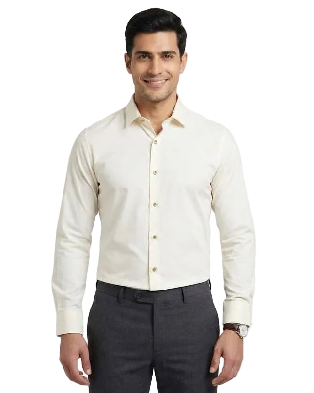 A man wearing a cream-colored long-sleeve button-down shirt and dark gray trousers, standing against a light gray studio background.