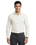 A man wearing a cream-colored long-sleeve button-down shirt and dark gray trousers, standing against a light gray studio background.